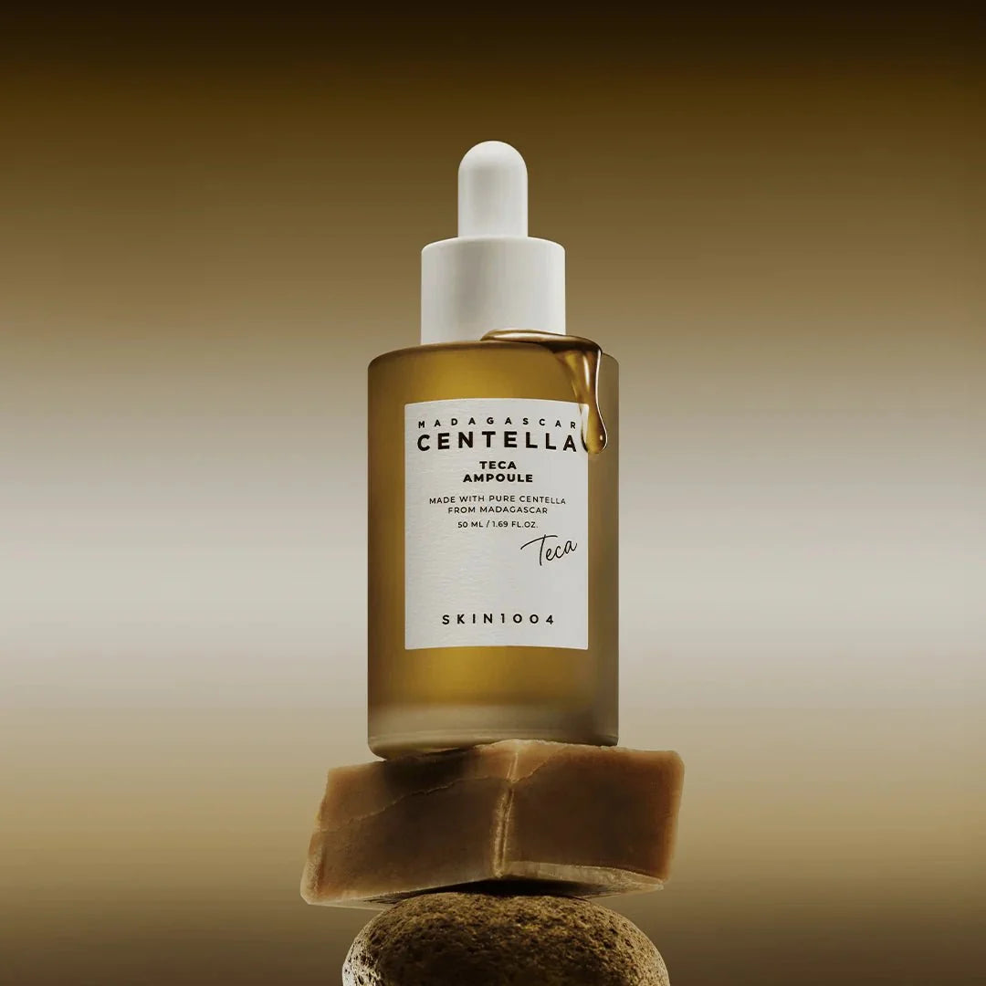 Skin1004 Centella Teca Ampoule bottle balanced on a natural stone with a golden liquid drip.